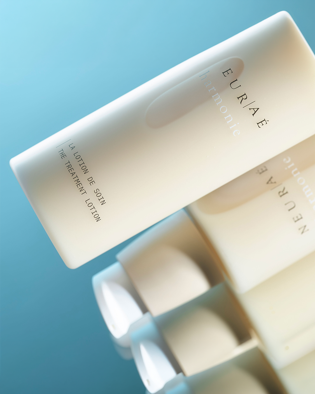The Neuraé Harmonie Treatment Lotion bottle angled on a glossy blue reflective surface with abstract mirrored reflections.