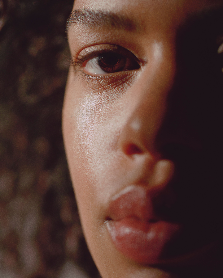 A dramatic close-up lifestyle portrait focusing on a person's glowing skin, captured in rich, warm, atmospheric lighting.