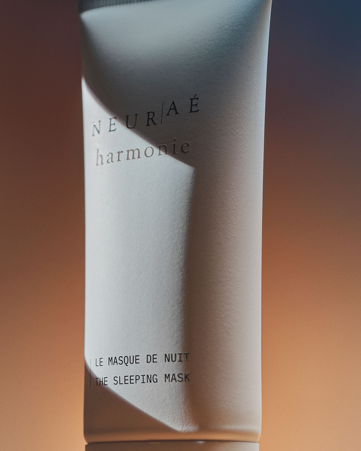 A dramatic, atmospheric close-up of the Neurae Harmonie The Sleeping Mask skincare tube highlighted by harsh, cinematic lighting.