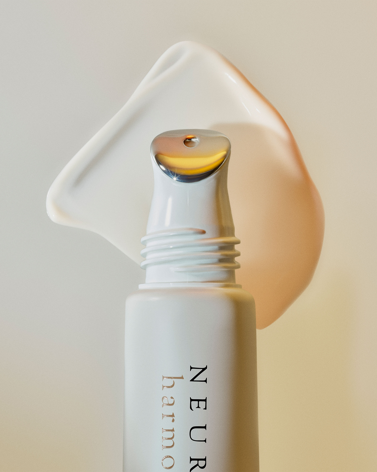 A close-up of a skincare pump bottle with a white cap and a clear dispensing tip showing a golden-yellow serum, set against a soft beige background with a white cream smear behind it. The bottle shows the brand name 'NEURAE' vertically.