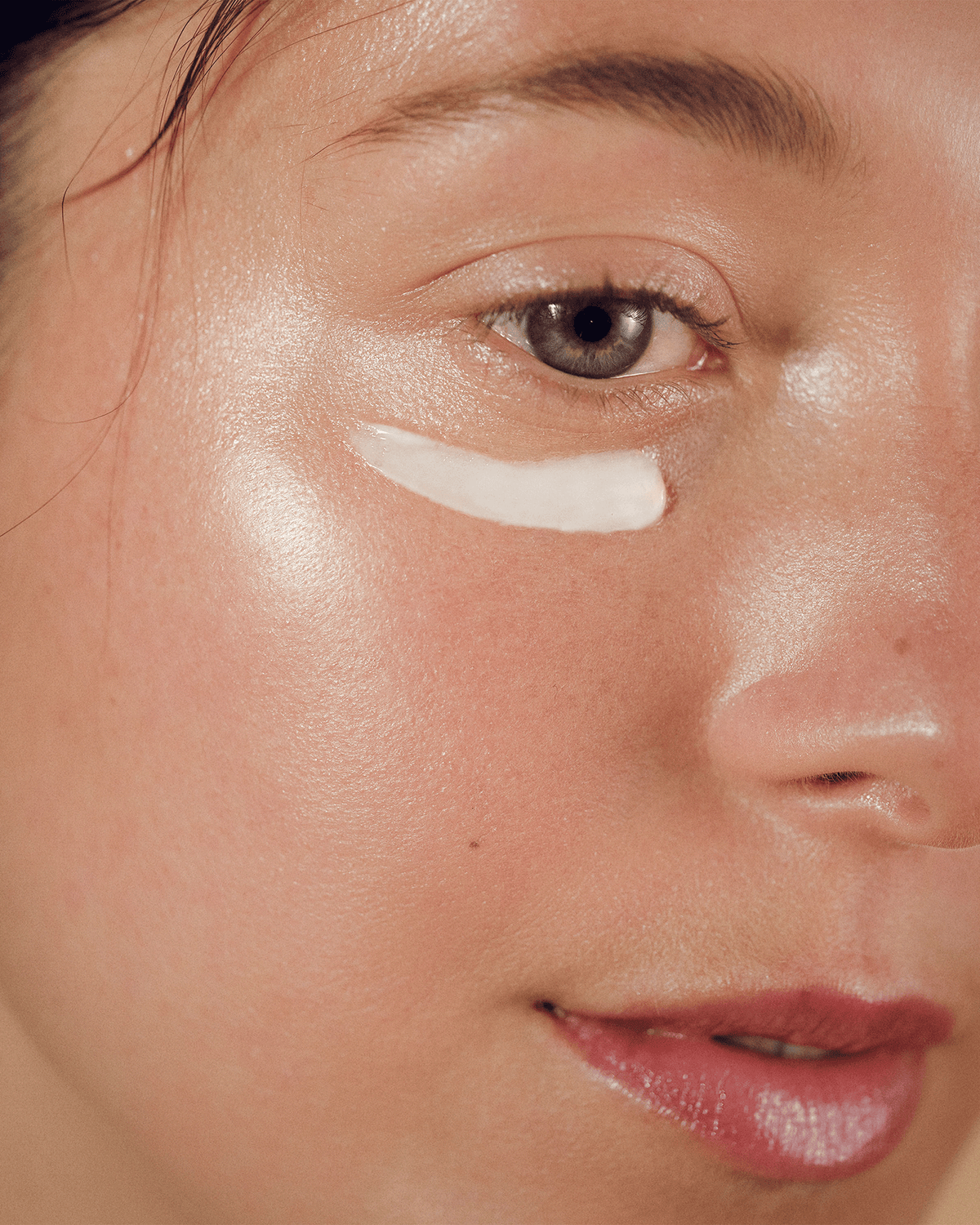 Close-up of a woman's face with a white cream makeup product applied in a curved stripe under her eye.