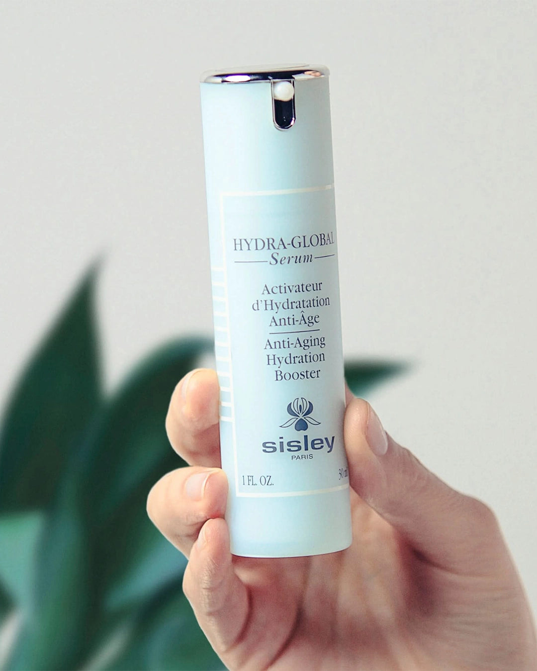 Hand holding a Sisley Hydra-Globale Serum bottle against a neutral background
