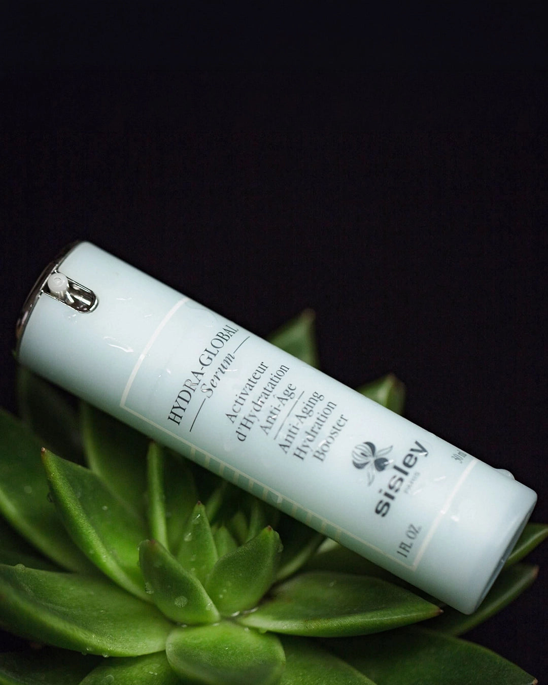 Sisley skincare product on a black background with green leaves