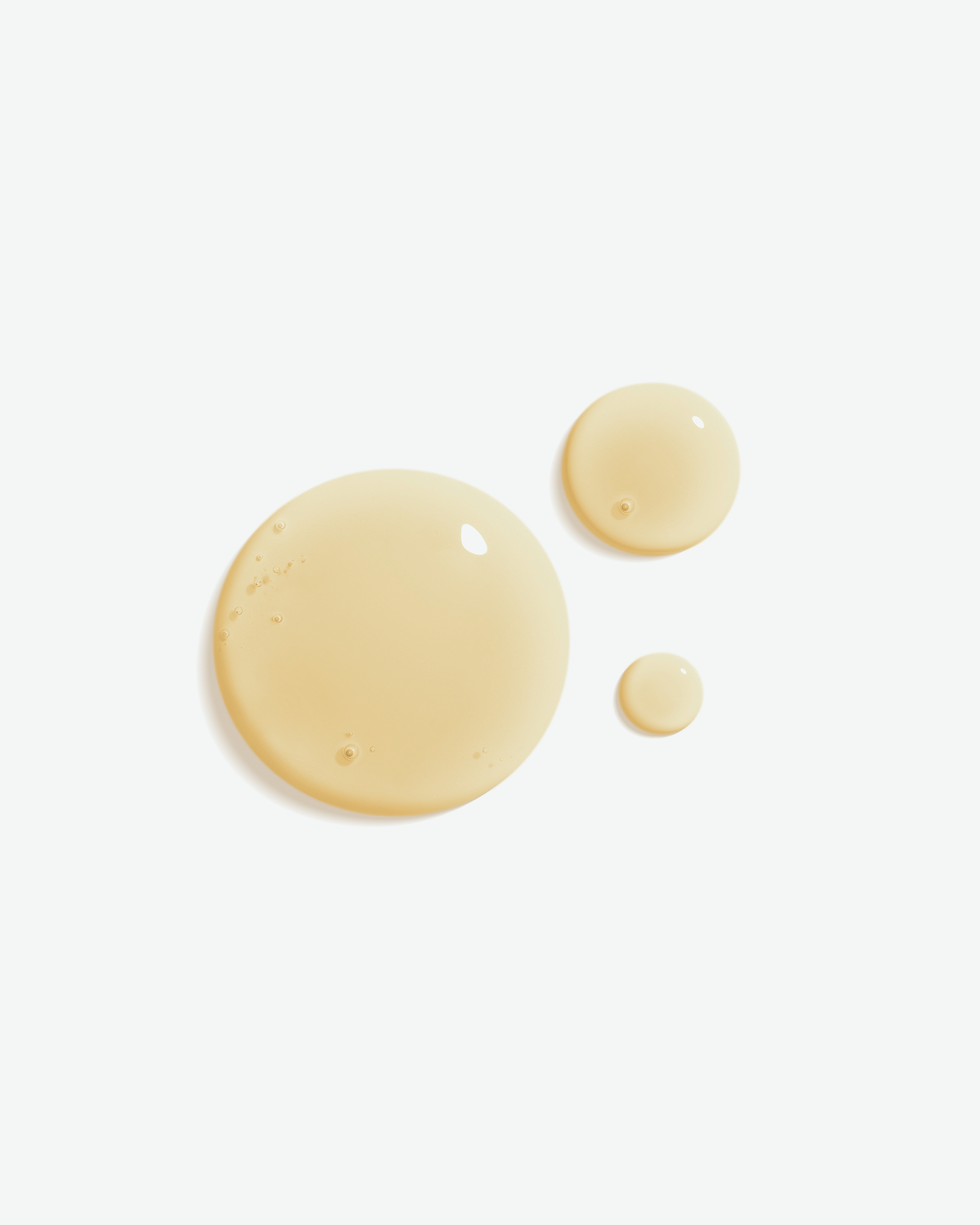 Three translucent droplets of a pale golden-yellow liquid, varying in size, arranged on a clean white background.