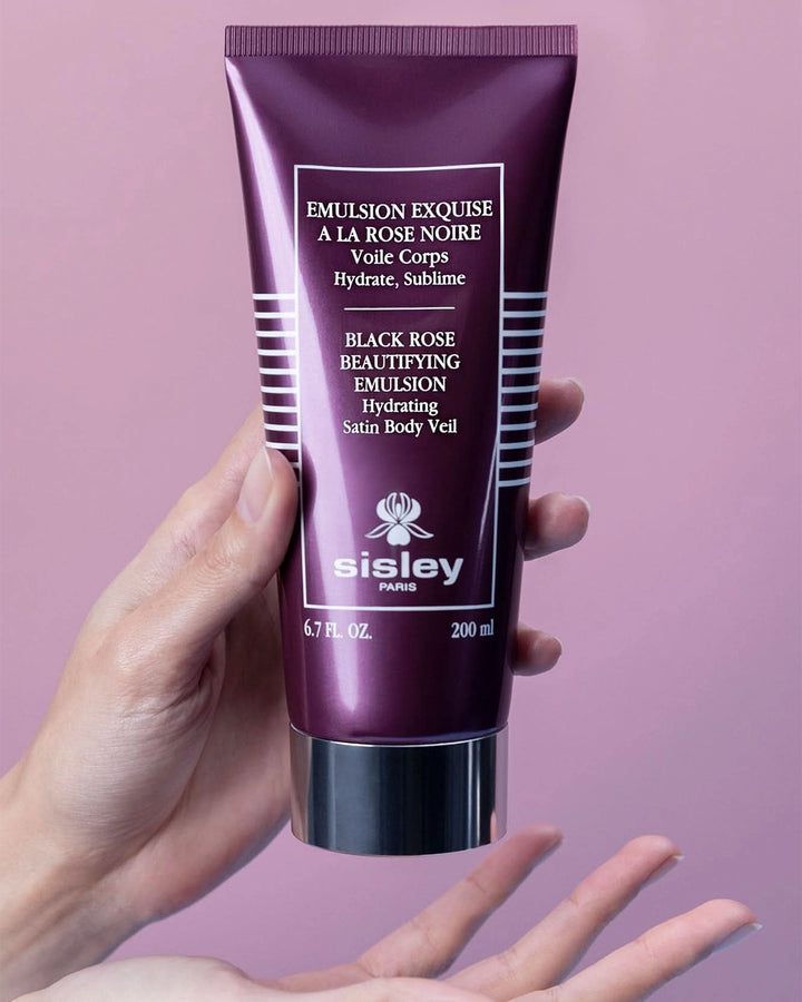 Hand holding a Sisley black rose emulsion tube against a pink background