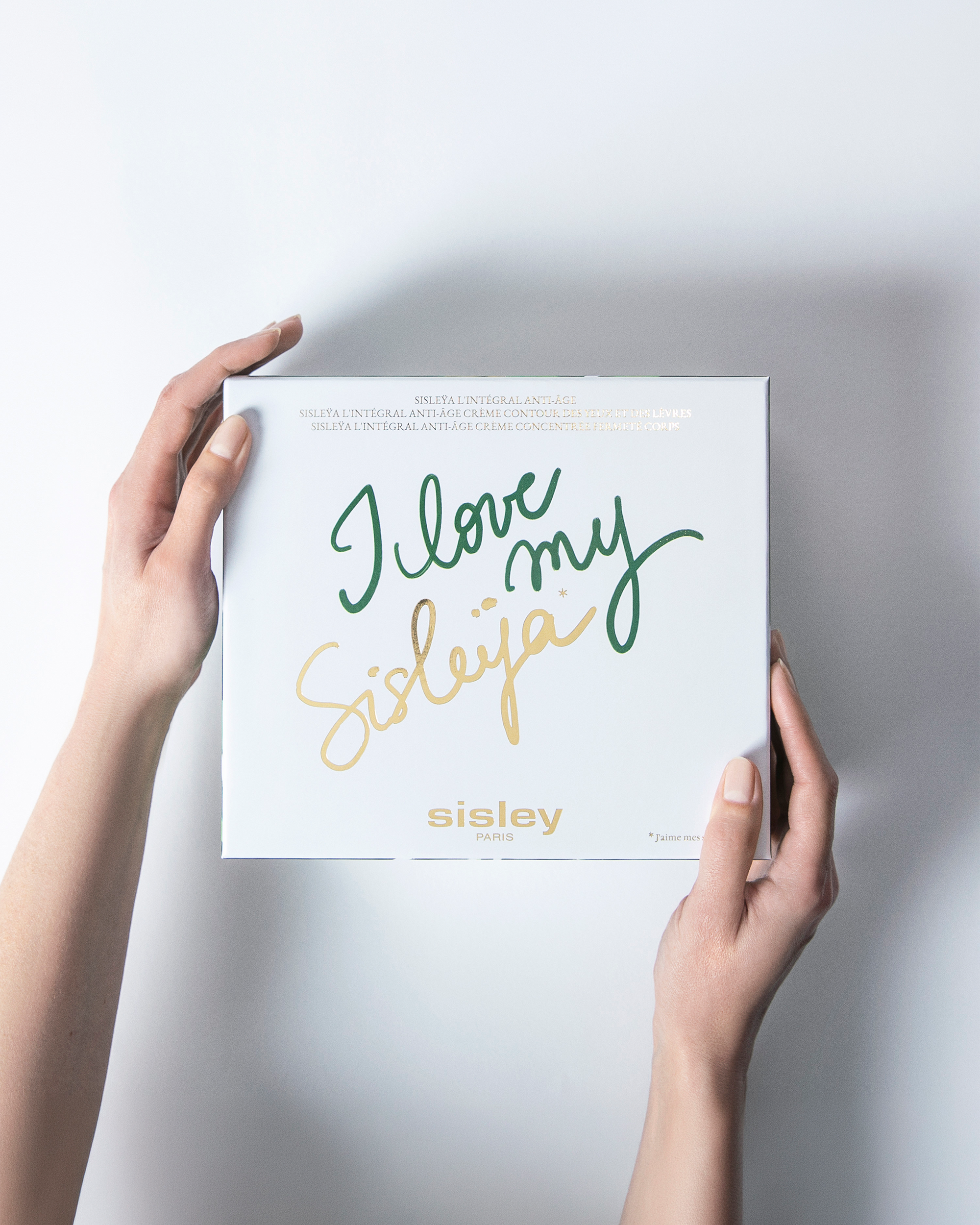 A person holds a white Sisley box with the phrase 'I love my Sisleyja' written in green and gold script, against a clean white background.