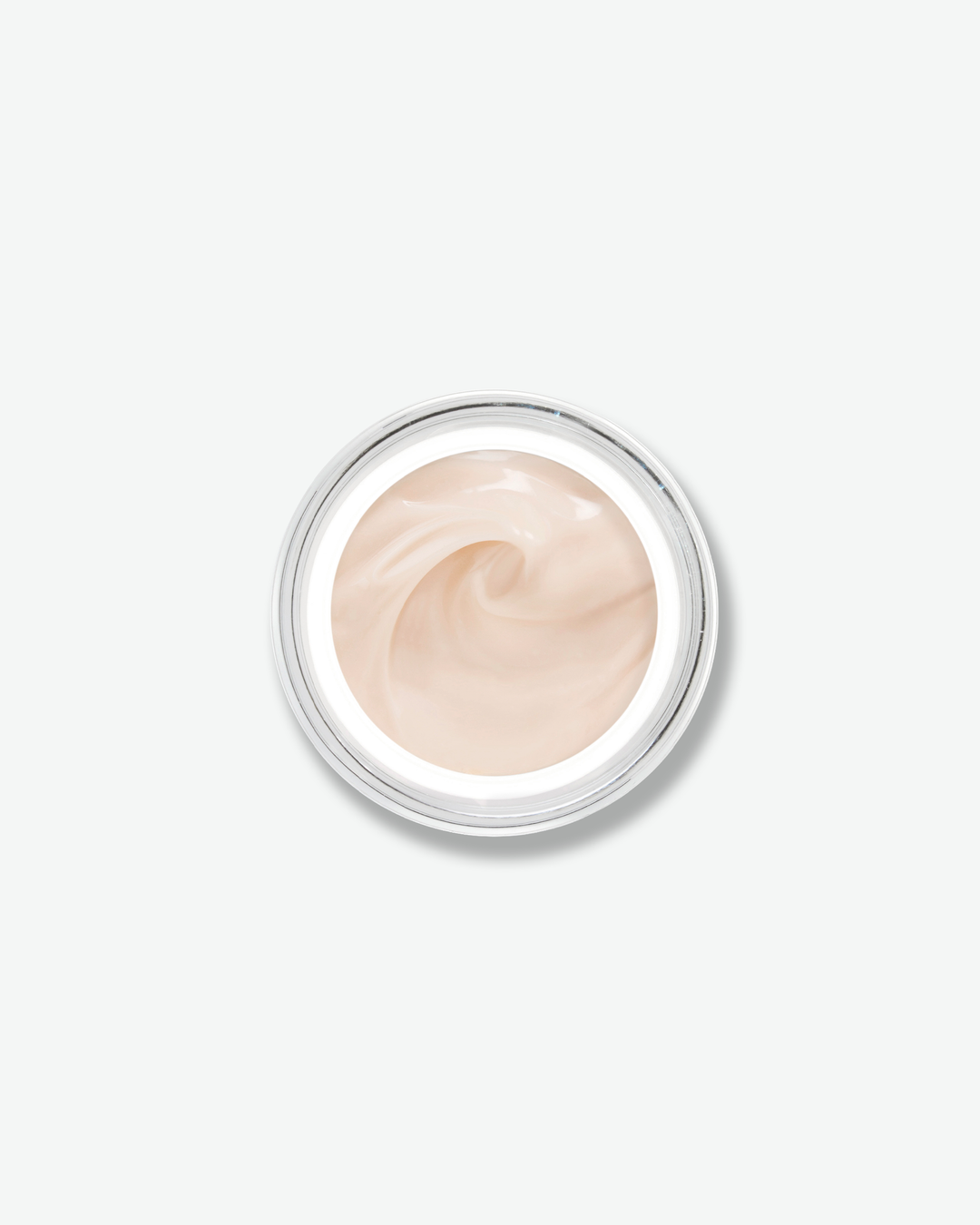 Overhead, top-down view looking directly into an open skincare jar against a plain gray background. The smooth, light-colored glass rim encircles a soft, pale peach-tinted face cream that is textured with an elegant swirl in the center.