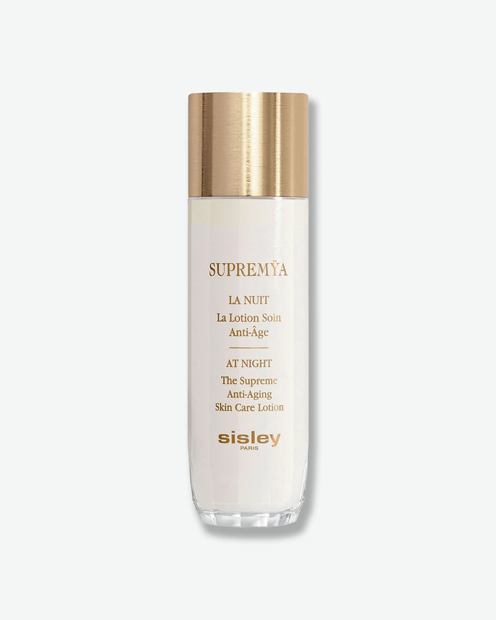 A tall, elegant white bottle of Sisley Paris Supremÿa At Night The Supreme Anti-Aging Skin Care Lotion, topped with a cylindrical brushed-gold cap.