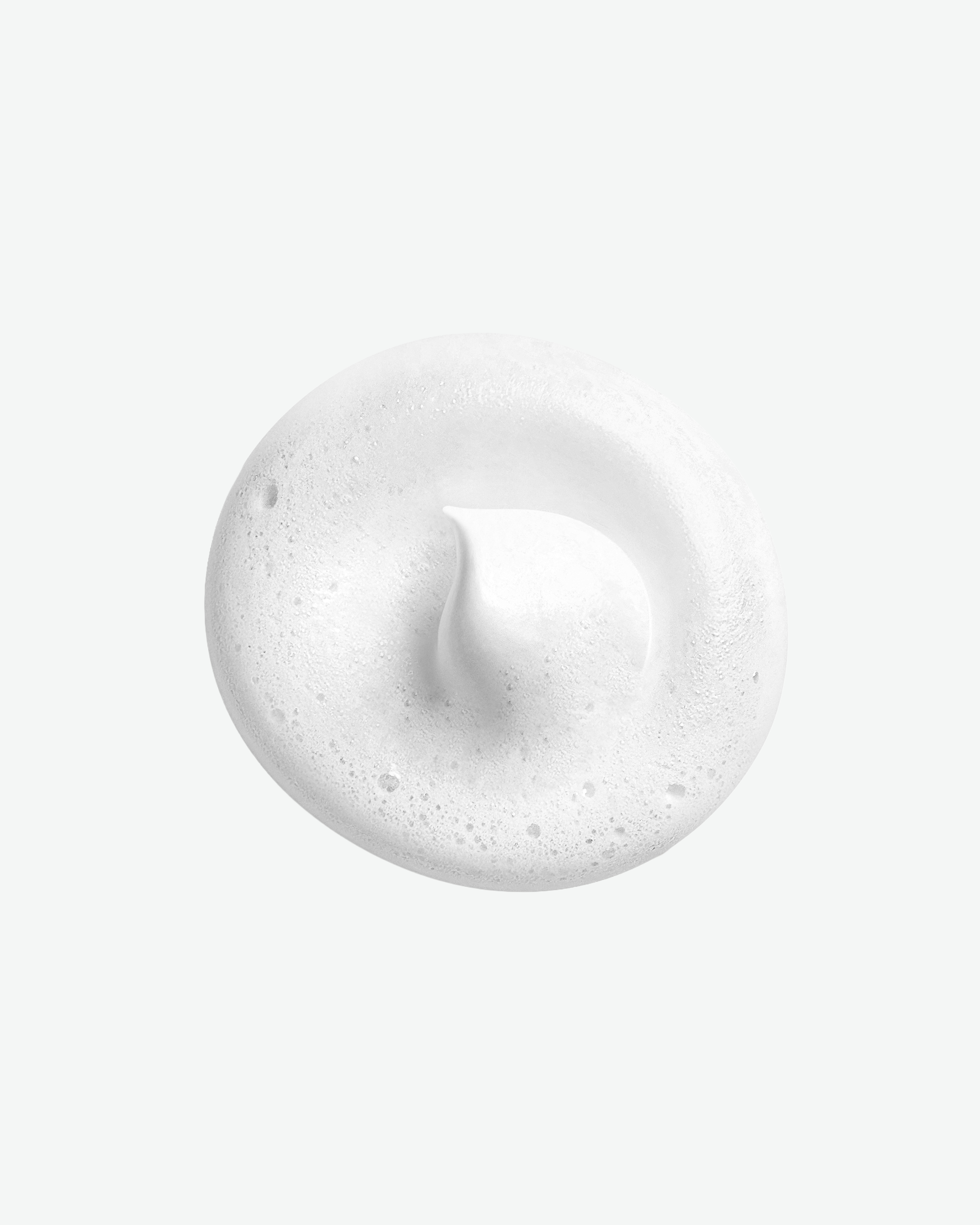 A circular dollop of soft white cosmetic foam with a small center peak, demonstrating product texture against a plain white background.