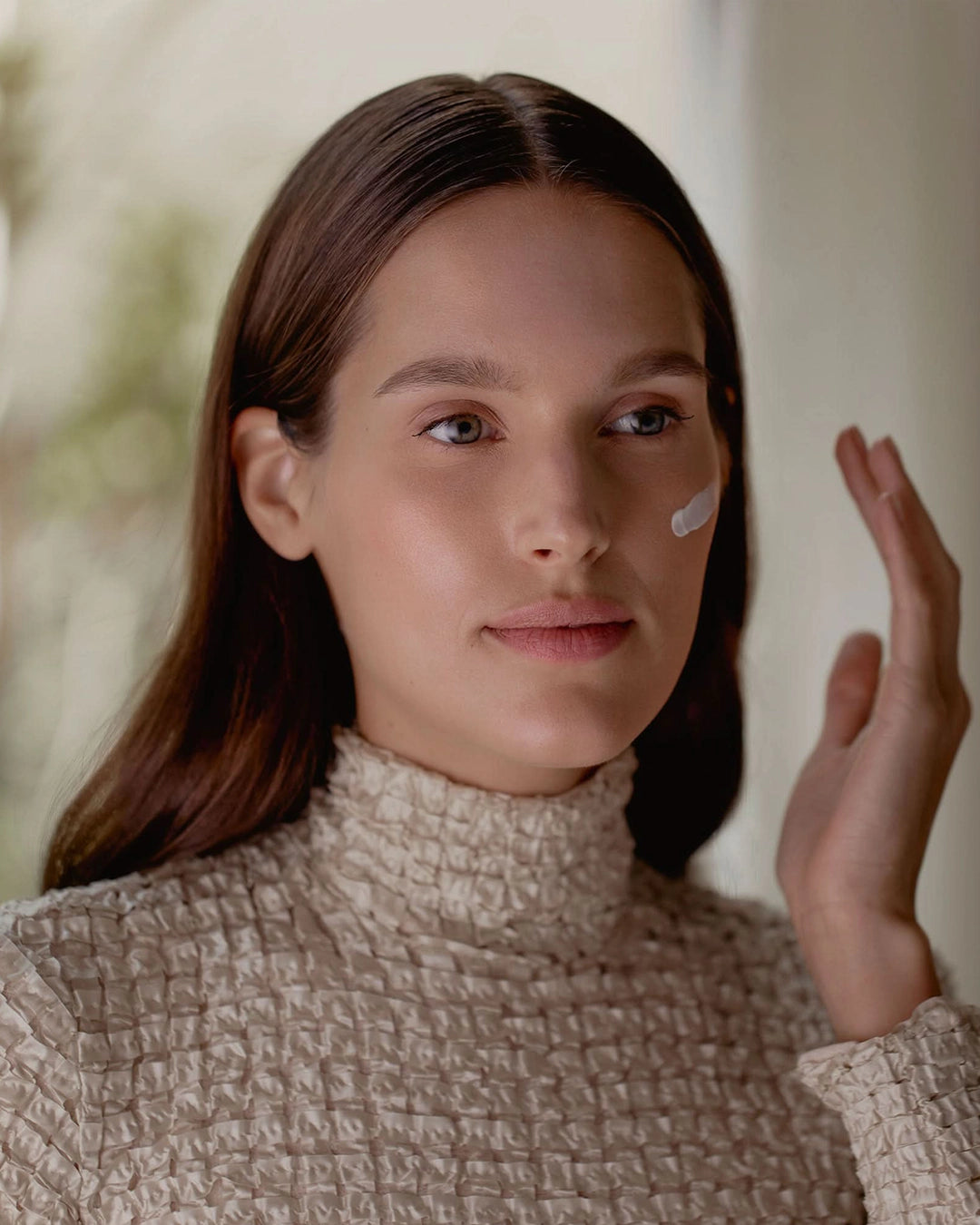 Woman applying cream to her face with a blurred background