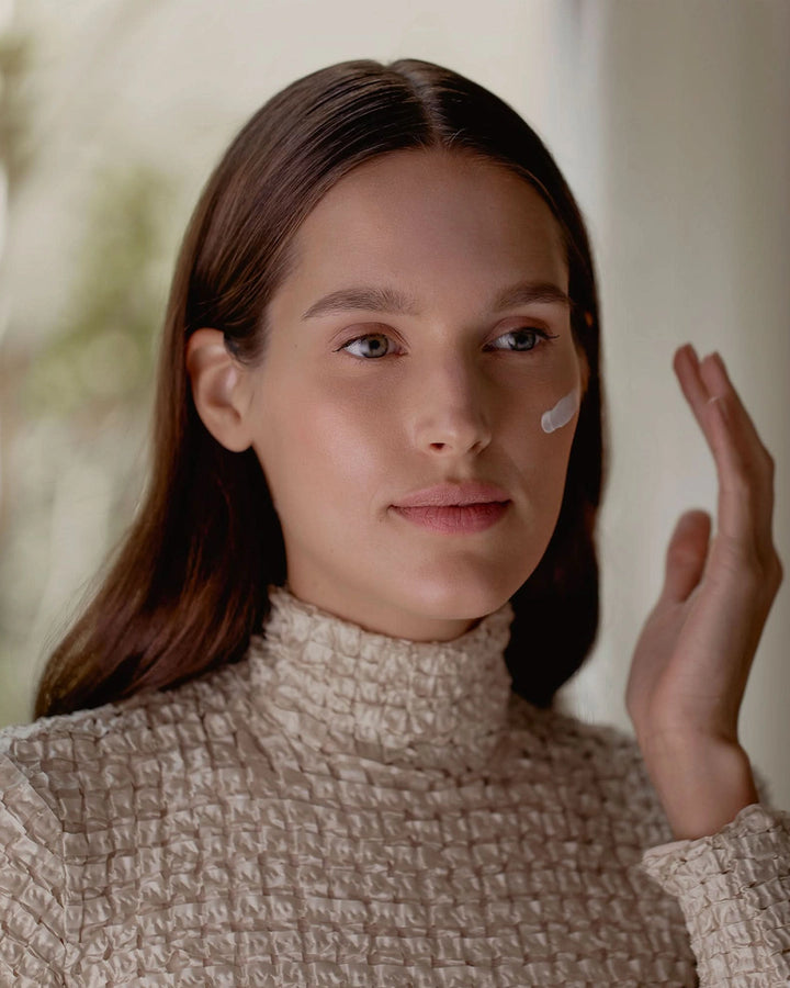 Woman applying cream to her face with a blurred background