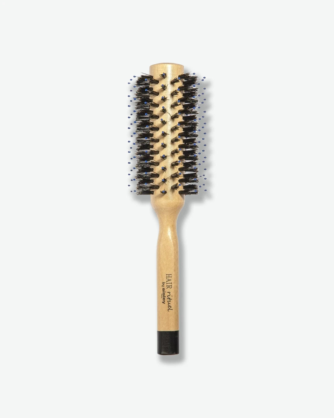 A top-down view of a HAIR Rituel by Sisley round blow-dry hairbrush, featuring a natural light-wood body and handle, dense black bristles mixed with blue ball-tipped pins, and a black base cap.