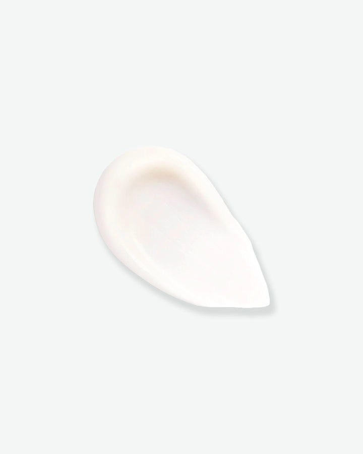 A smooth, thick teardrop-shaped swipe of creamy white makeup primer showcasing its soft matte texture against a light background.