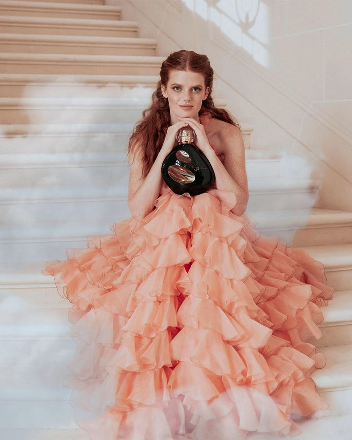 Woman in a peach ruffled dress holding a sisley perfume on a staircase.