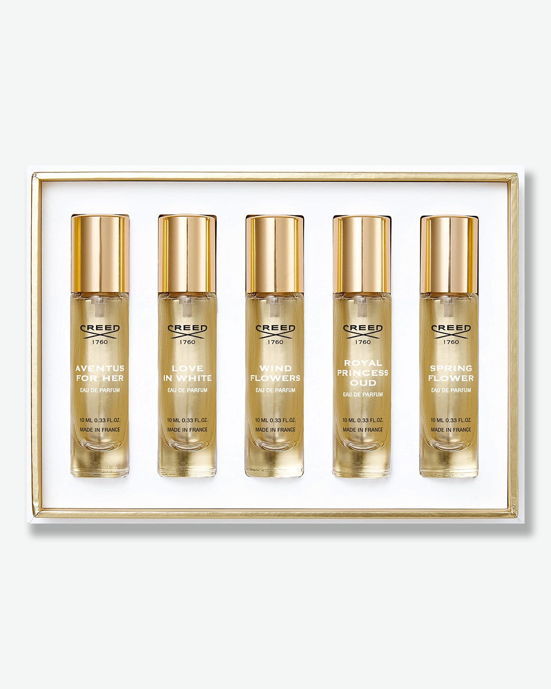 A Creed luxury perfume gift set shown from a top-down view. Nestled in a gold-bordered white tray, are five identical clear glass travel spray bottles with gold caps. From left to right, the bottles are labeled "Aventus for Her", "Love in White", "Wind Flowers," "Royal Princess Oud," and "Spring Flower," each marked as 10 ml Eau de Parfum made in France.