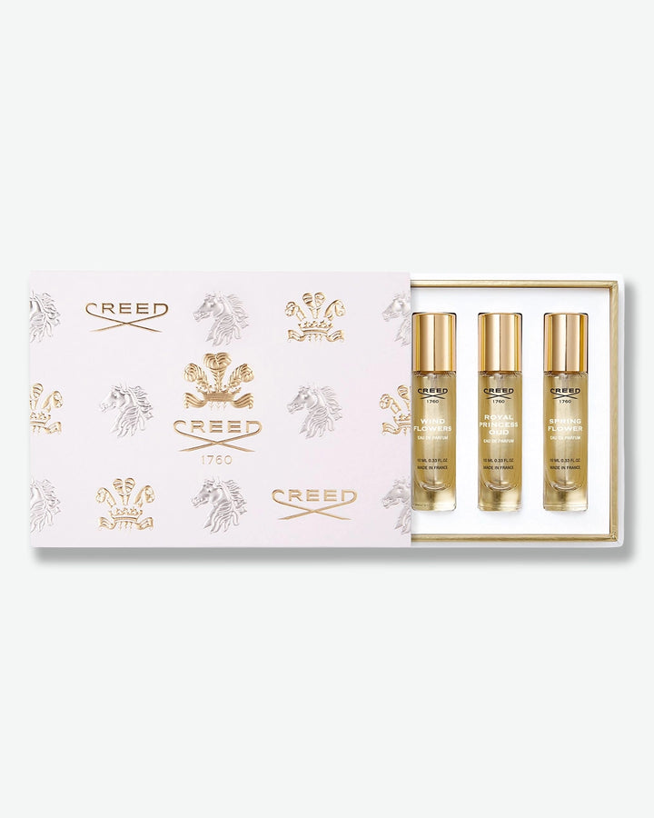 Creed fragrance discovery gift set featuring a white and gold embossed presentation box slid open to reveal three 10 ml travel spray bottles: Wind Flowers, Royal Princess Oud, and Spring Flower.