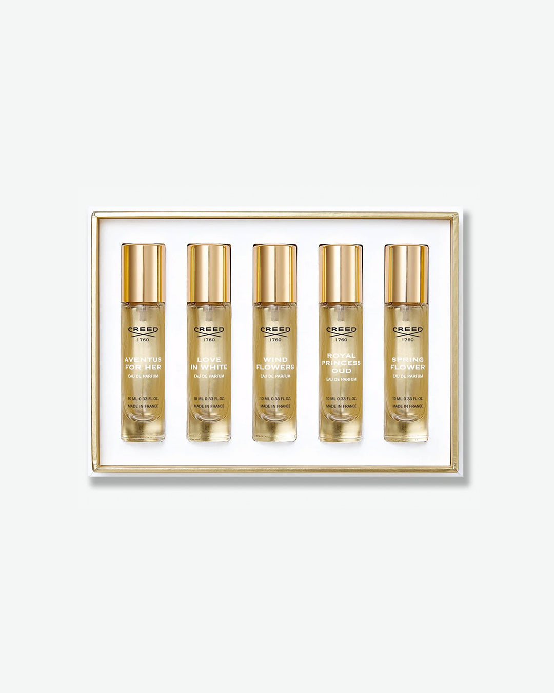 A Creed fragrance discovery set displaying five travel spray vials in a white box with a thin gold inner border, featuring scents like Aventus for Her, Love in White, and Wind Flowers, isolated on a light grey background.