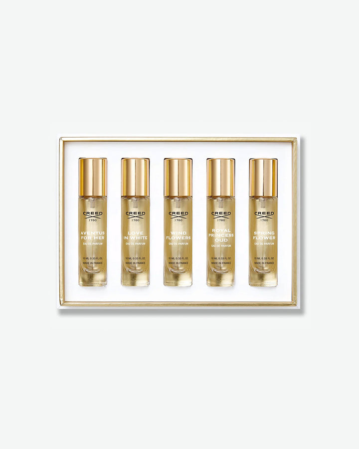 A Creed fragrance discovery set displaying five travel spray vials in a white box with a thin gold inner border, featuring scents like Aventus for Her, Love in White, and Wind Flowers, isolated on a light grey background.