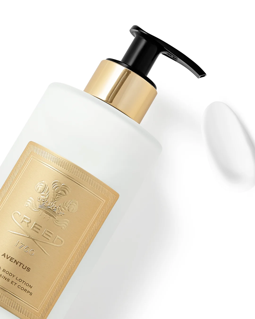 White Creed Aventus Hand & Body lotion bottle with black pump and gold label, next to a white texture swatch, on a white background