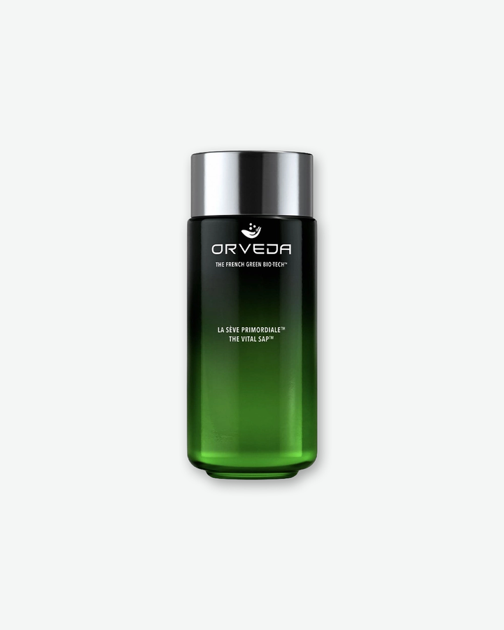 A product shot of an Orveda The Vital Sap bottle, centered against a plain light gray background. The sleek, tall cylindrical glass bottle features a deep ombre green gradient that transitions from a dark, near-black top to a translucent emerald green base. It is sealed with a metallic silver screw cap, and the front displays the white Orveda logo, "THE FRENCH GREEN BIO-TECH™", and the product name "LA SÈVE PRIMORDIALE™ THE VITAL SAP™".