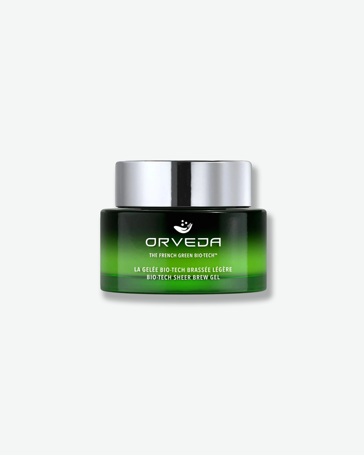 Front view of an Orveda "Bio-Tech Sheer Brew Gel" jar against a plain gray background. The cylindrical green glass container displays a dark gradient blending into an emerald green base, featuring white product descriptions and topped with a flat silver cap.