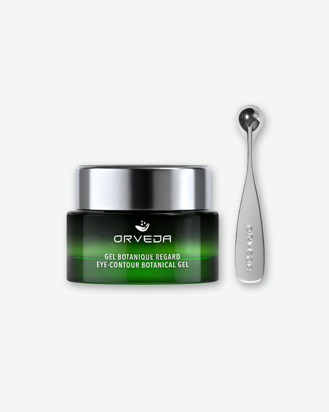 Product shot showcasing a compact Orveda "Eye-Contour Botanical Gel" jar paired with its application tool against a plain gray background. The small glass jar features a green ombre design and a silver lid, standing beside a sleek, matching silver metallic massage spatula.