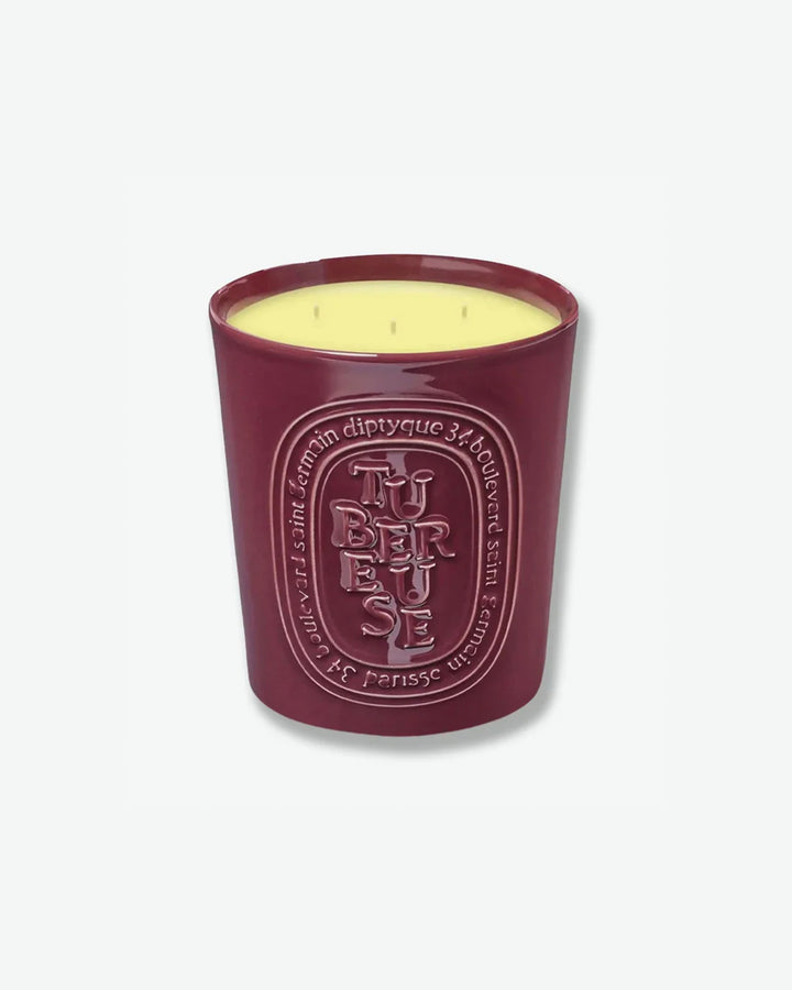 Diptyque Tubéreuse multi-wick scented candle in a glossy, dark plum-colored ceramic vessel featuring an embossed oval logo, isolated on a light grey background.