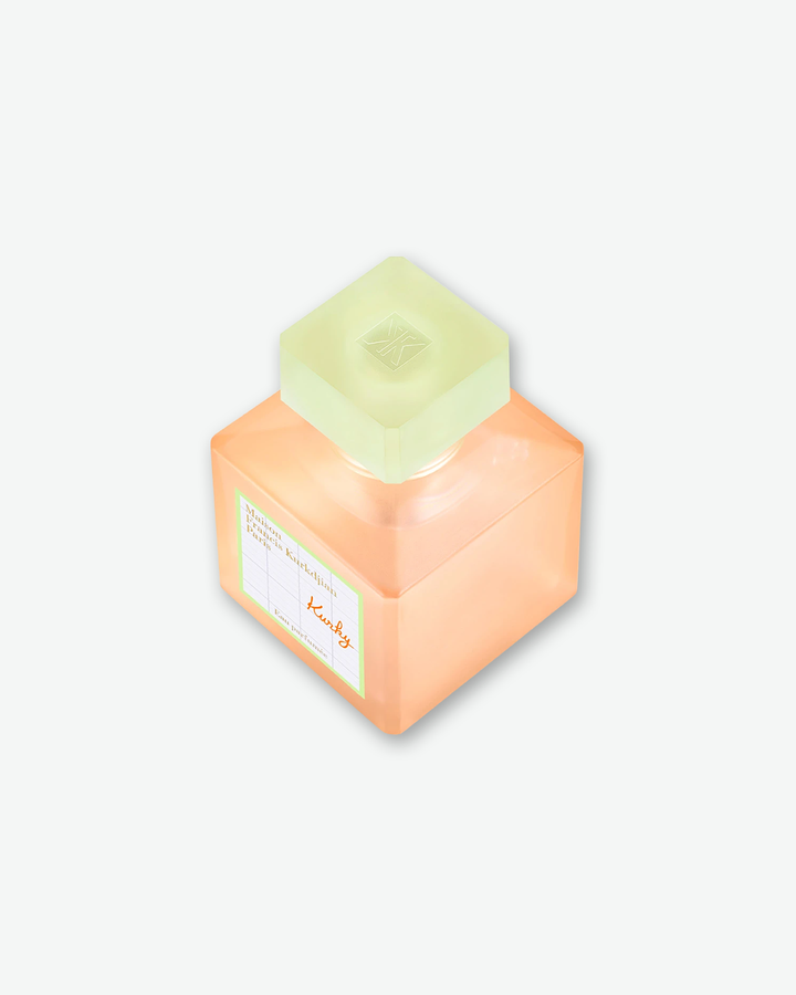 An elevated, three-quarter angled view of the square Maison Francis Kurkdjian Paris "Kurky" Eau Parfumée bottle. The shot highlights the translucent, frosted lime green square cap embossed with the brand's monogram logo on top.