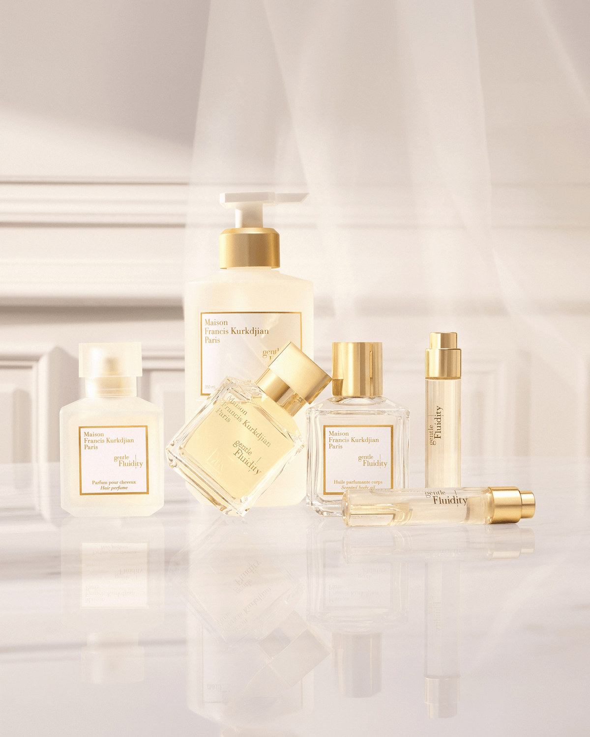 Maison Francis Kurkdjian Gentle Fluidity collection arranged on a reflective surface in a softly lit cream interior, featuring fragrance, body oil, hair perfume, and travel formats.