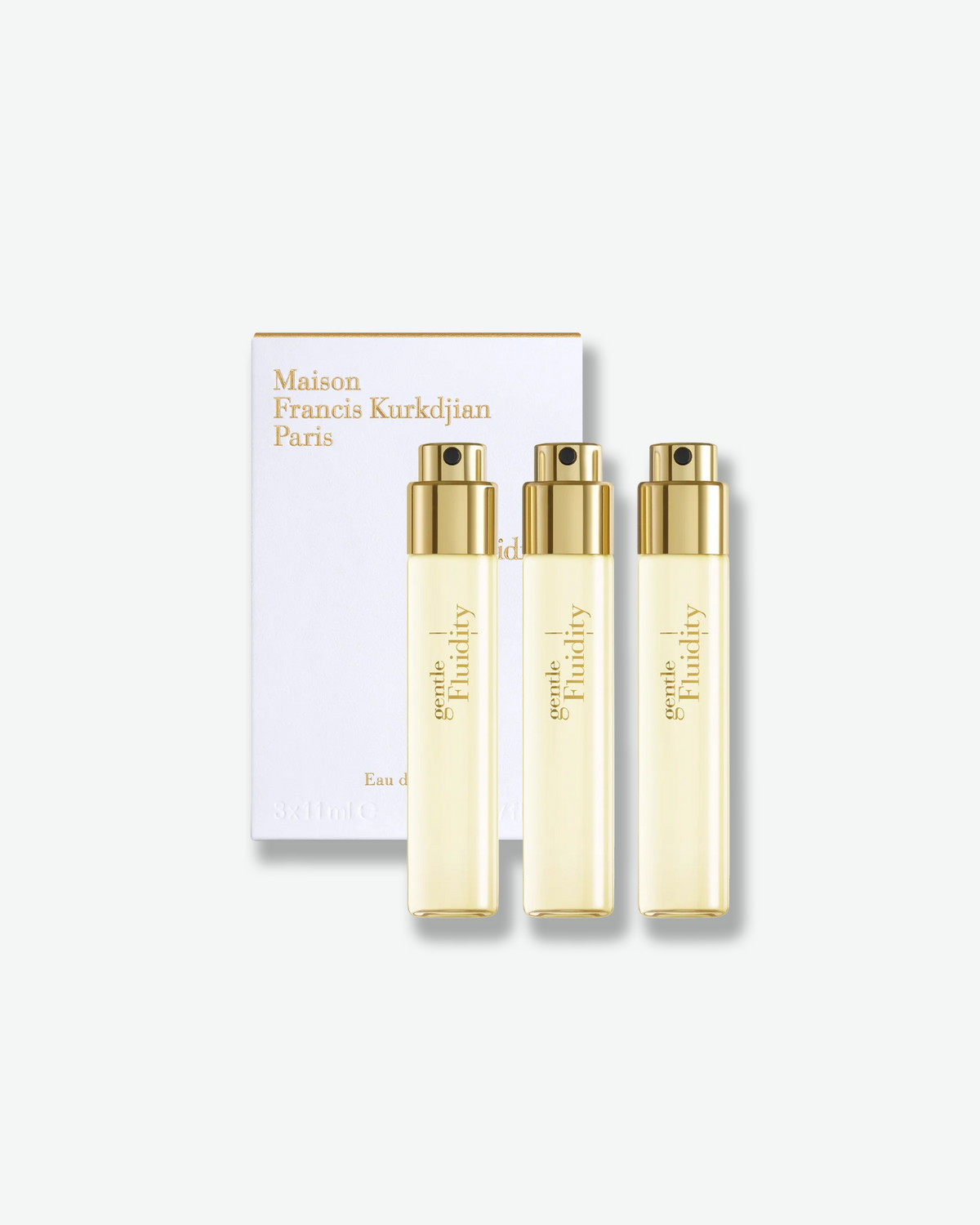 Three Gentle Fluidity Gold Eau de Parfum travel sprays with gold atomizers, displayed in front of a white Maison Francis Kurkdjian Paris gift box with gold lettering.