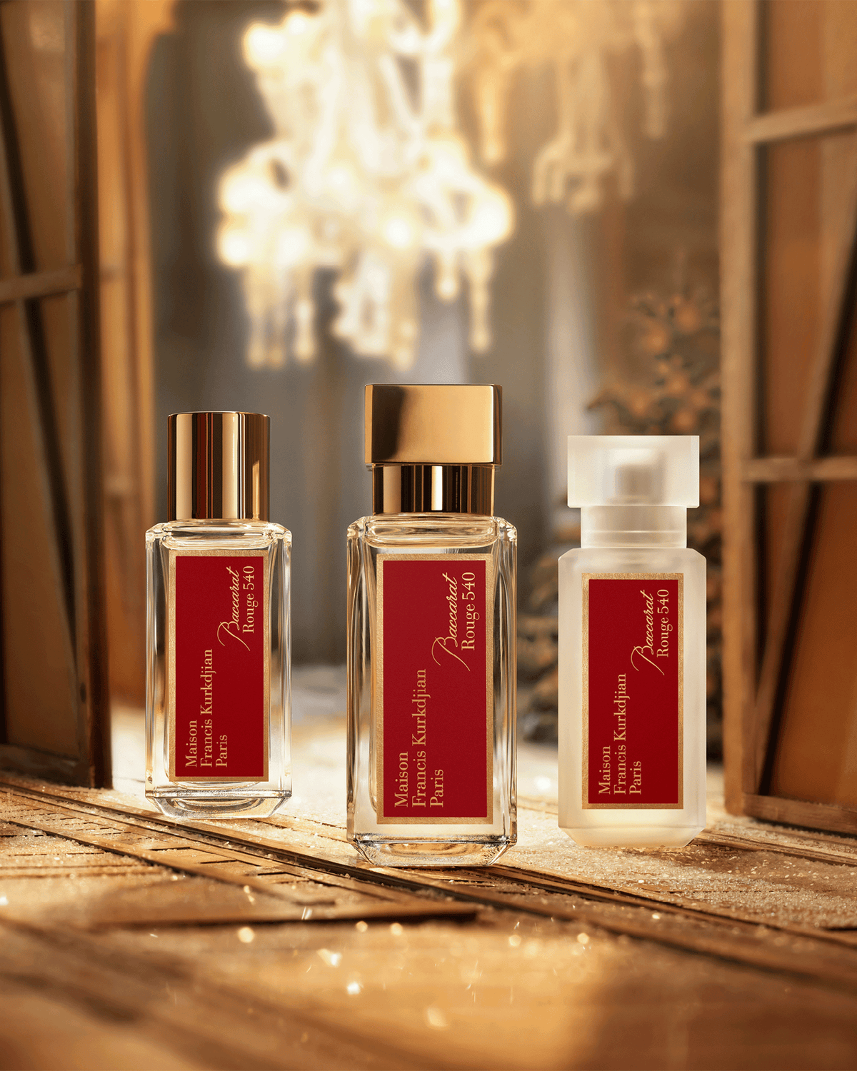 Three Maison Francis Kurkdjian Baccarat Rouge 540 fragrance ritual products displayed on a reflective gold surface with warm lighting and a chandelier in the background.