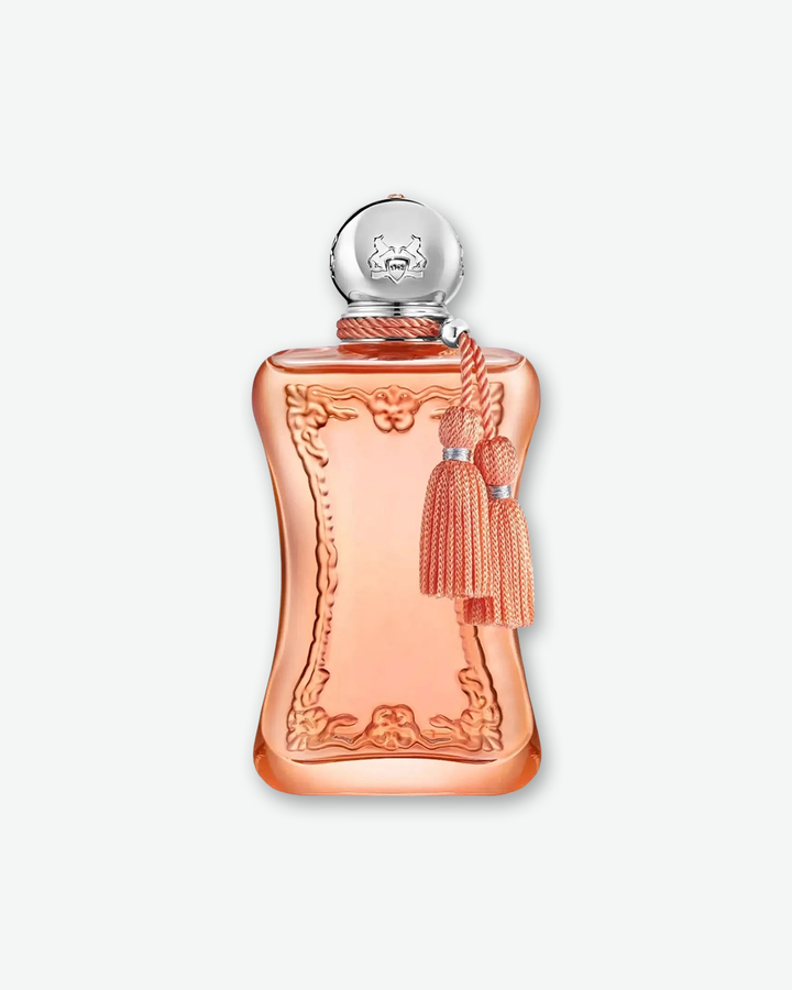 A studio product shot of a Parfums de Marly fragrance bottle against a light gray background. The translucent glass bottle is filled with a soft peach-pink perfume, featuring an elegant, curved hourglass silhouette adorned with raised baroque-style molding on the front. A spherical silver cap engraved with a horse crest sits on top, with a matching peach twisted cord wrapped around the neck that holds two decorative tassels.