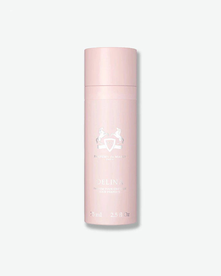 A studio product shot of Parfums de Marly Delina Hair Perfume against a light gray background. The sleek, cylindrical spray bottle features a solid, light pastel pink finish with a matching cap. The front is detailed with an embossed silver equestrian crest and the name 'DELINA PARFUM POUR CHEVEUX HAIR PERFUME' in metallic silver text.