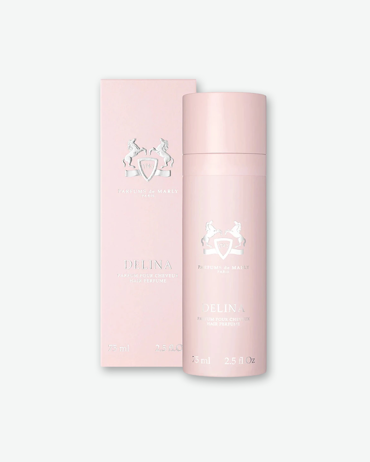 A product presentation shot showing a Parfums de Marly Delina Hair Perfume bottle standing in front of its soft pink packaging box. Both items display matching silver embossed brand details, featuring the iconic equestrian crest logo, brand name, and 'DELINA HAIR PERFUME' centered on a clean, pastel pink background.