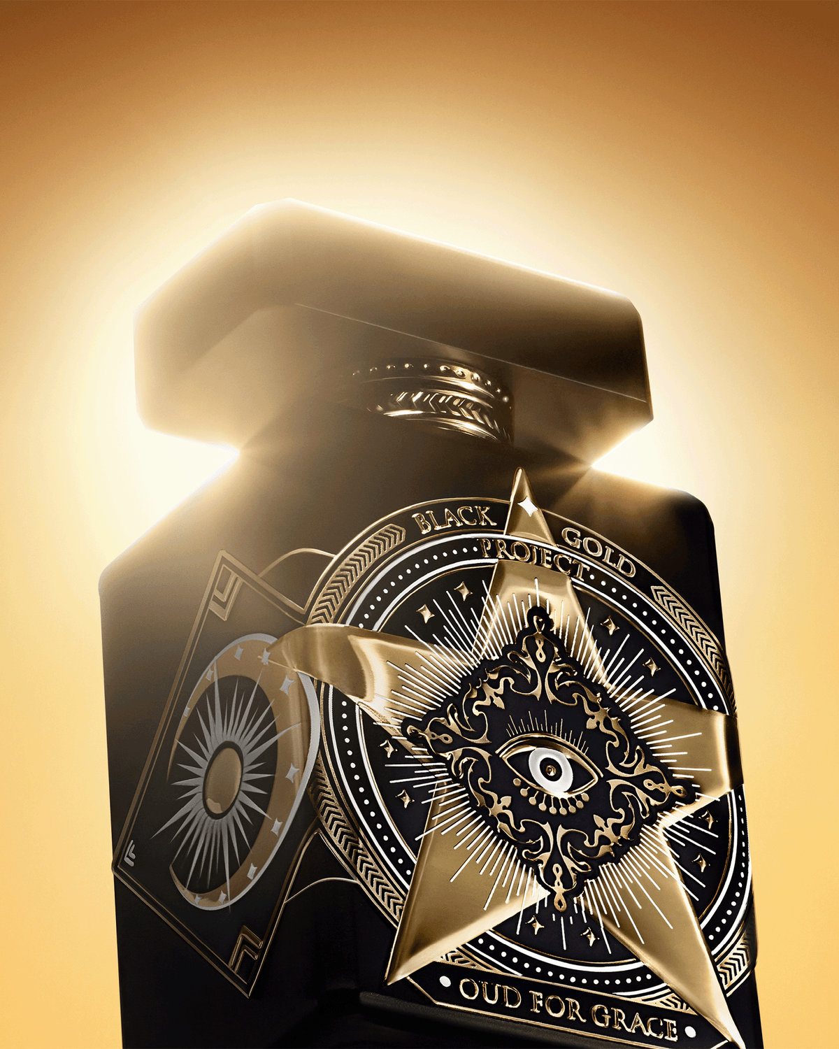 Close-up of Initio Oud for Greatness Black Gold Project fragrance bottle with ornate gold detailing against a glowing golden background.