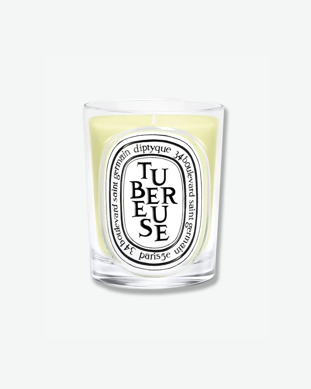 Diptyque Tubéreuse scented candle showcasing light yellow-tinted wax in a classic clear glass jar with the signature white oval logo, isolated on a light grey background.
