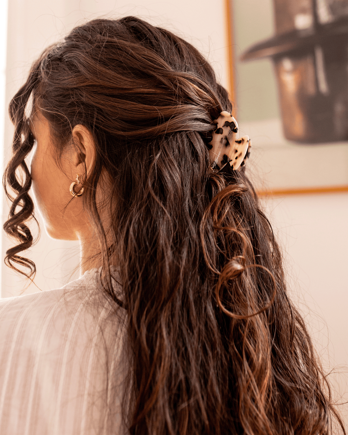 Side view of a model with long, wavy brown hair styled half-up and secured with a tortoiseshell Bachca hair claw clip.
