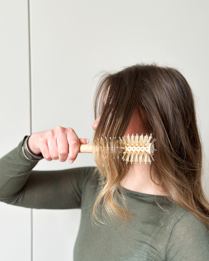 Person holding a hairbrush in front of their face against a plain background