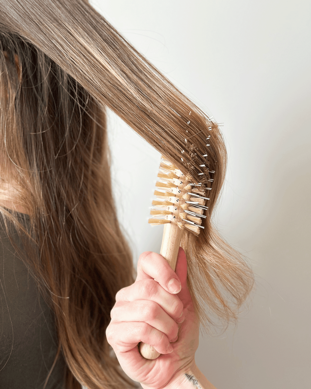 Person holding a hairbrush with long hair, against a neutral background