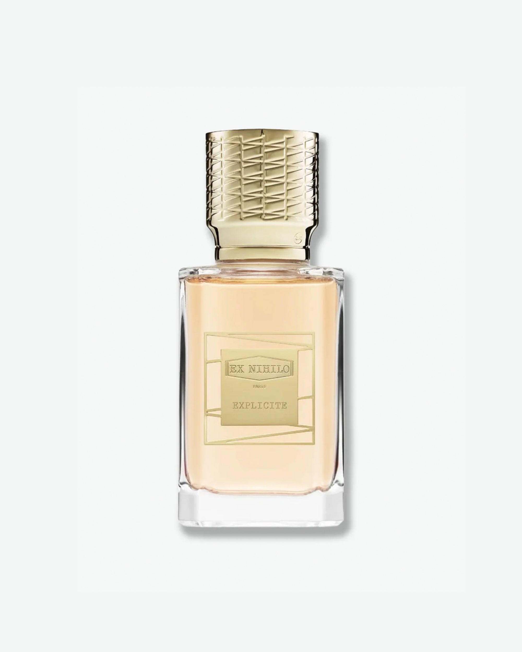 Product shot of Ex Nihilo Explicite Eau de Parfum. The fragrance is housed in a clear rectangular glass bottle showcasing a soft peach-colored juice. It features an ornate, gold-engraved cap with a geometric lattice pattern and a central gold geometric label, casting a subtle shadow against a minimal light grey background.