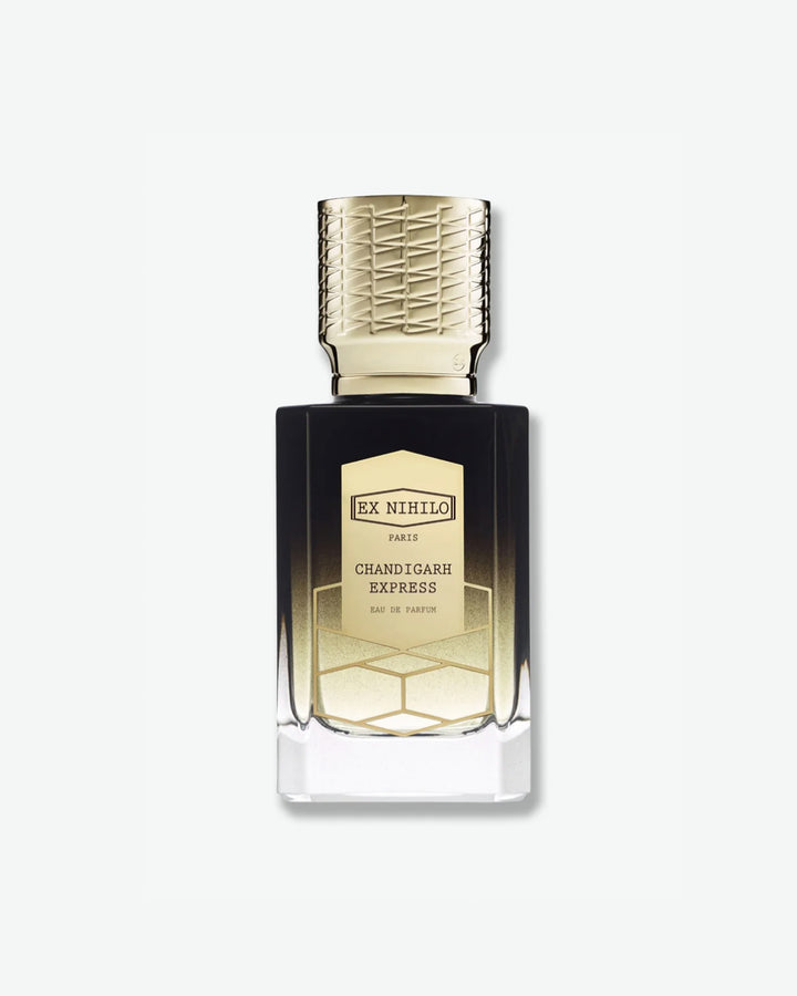 Ex Nihilo Chandigarh Express Eau de Parfum in a luxurious glass bottle with a dark brown to clear ombré finish, topped with an intricately engraved gold cap and a gold geometric label, isolated on a light grey background.