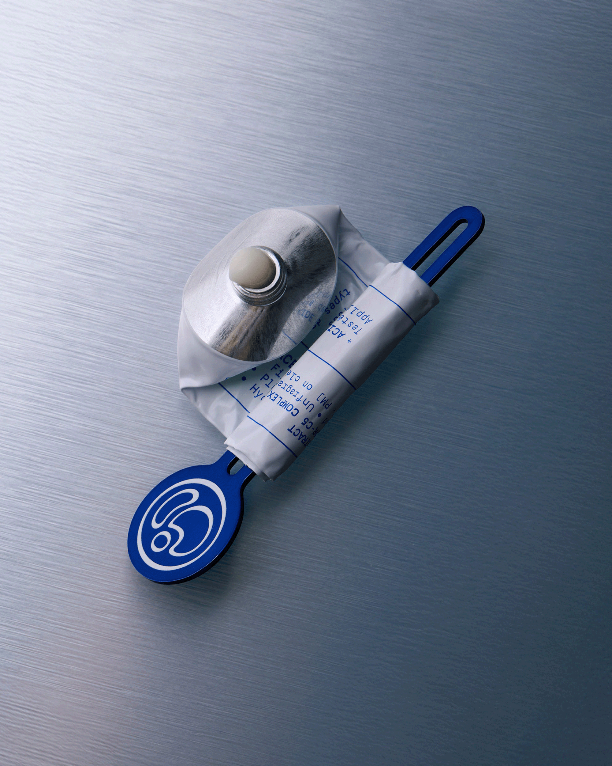 A medical oxygen mask with a blue handle and a crumpled white oxygen cylinder tube, photographed on a brushed metallic blue-gray surface.