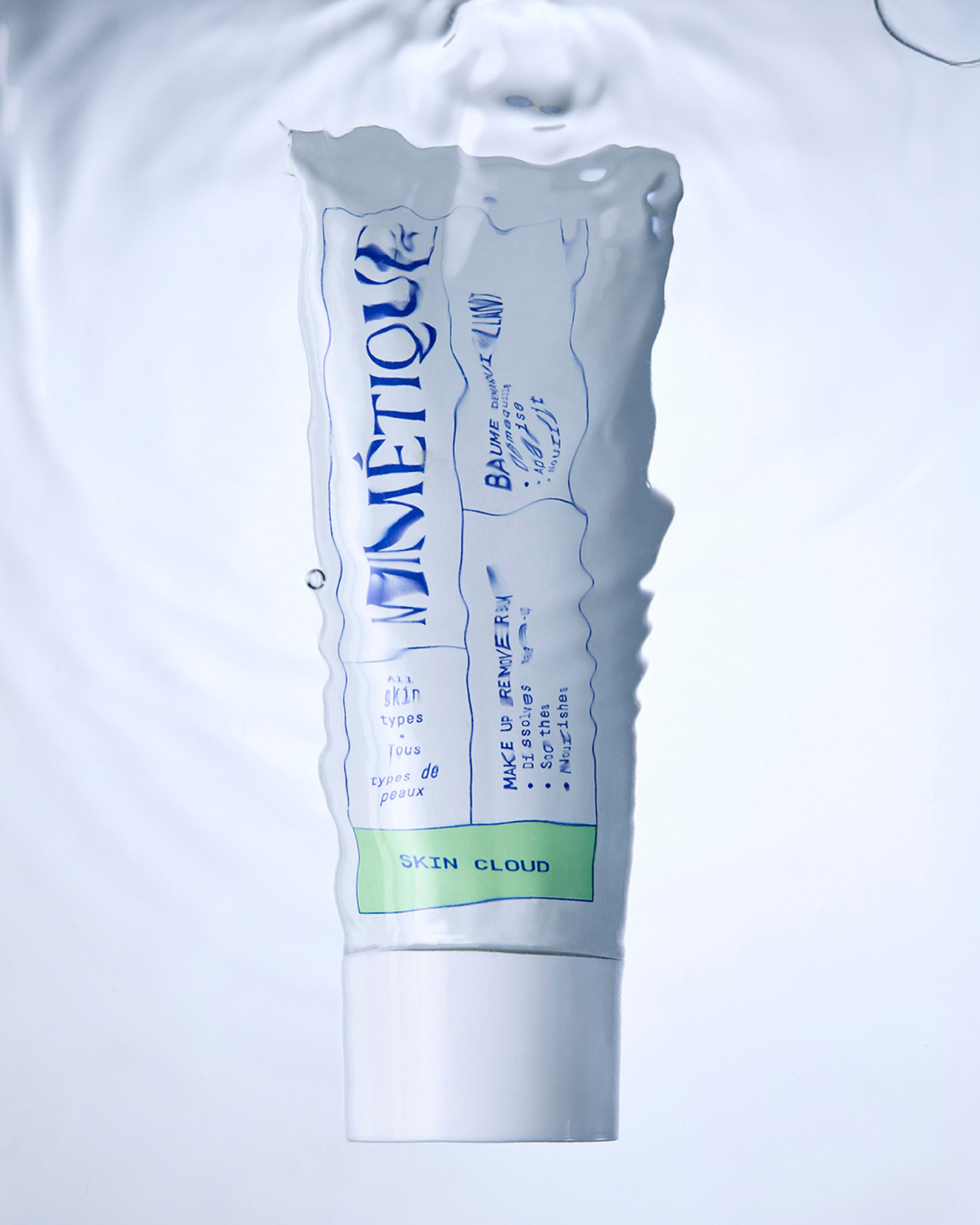 A squeeze tube of Minétique Balmy Cloud hand cream, featuring a white body with blue text and a light green band at the bottom, set against a water ripple background.