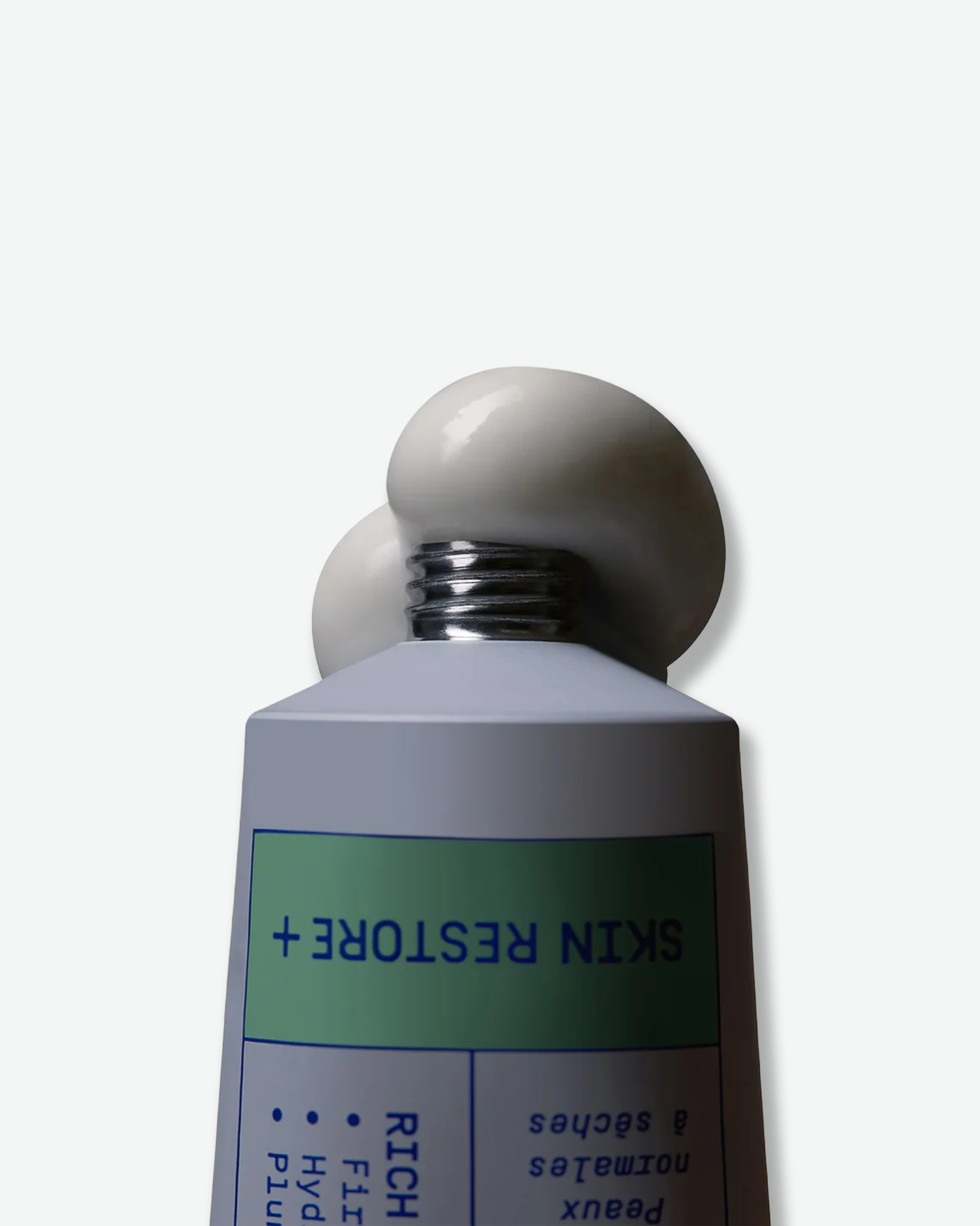 A close-up of a squeeze tube of skincare cream with white cream puffed out of the open top against a clean white background.