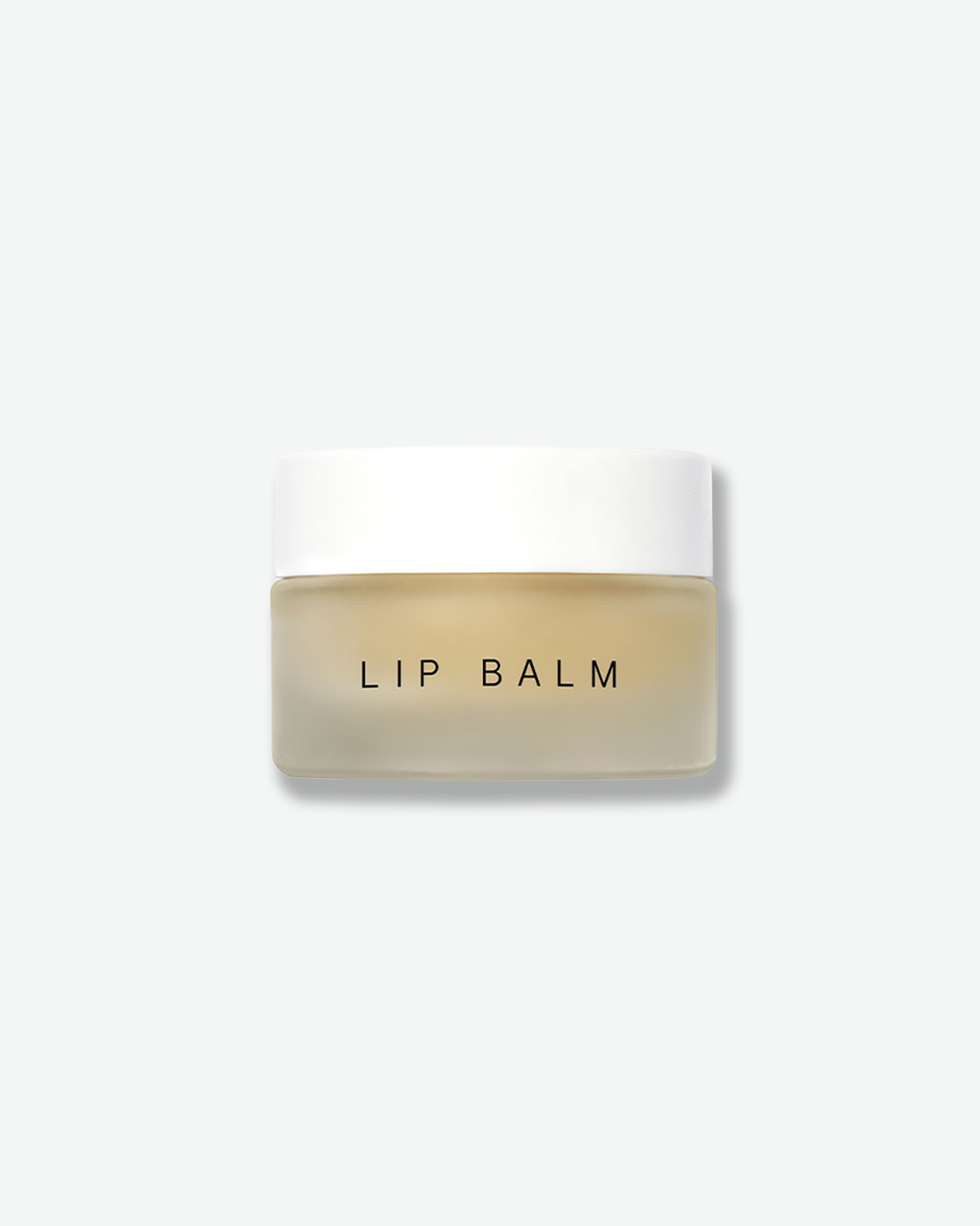 Front view of a Dr. Barbara Sturm Lip Balm jar against a plain gray background. The small, minimalist container features a frosted clear glass base showcasing the pale yellow balm inside, with the words "LIP BALM" printed in a clean black sans-serif font across the front, topped with a smooth white cap.