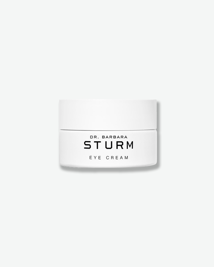 A product shot of a Dr. Barbara Sturm Eye Cream jar, centered against a light gray background. The white cylindrical jar features a matching flat white cap. The front displays clean, minimalist black text that reads "DR. BARBARA STURM" and "EYE CREAM".
