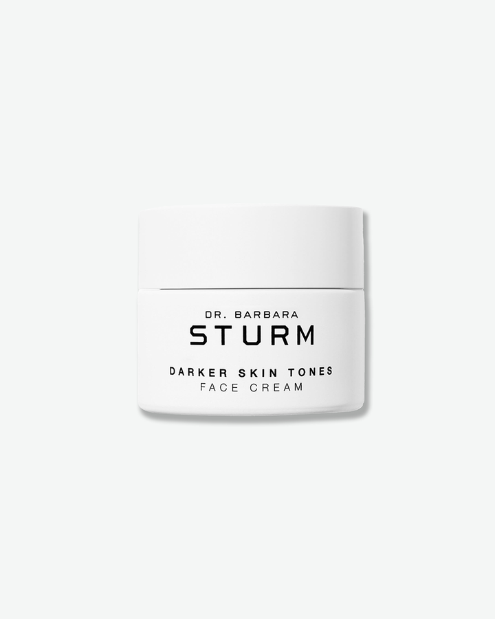 A product shot of a Dr. Barbara Sturm Darker Skin Tones Face Cream jar, centered against a light gray background. The white cylindrical jar has a matching flat screw cap and features black text on the front reading "DR. BARBARA STURM" and "DARKER SKIN TONES FACE CREAM".