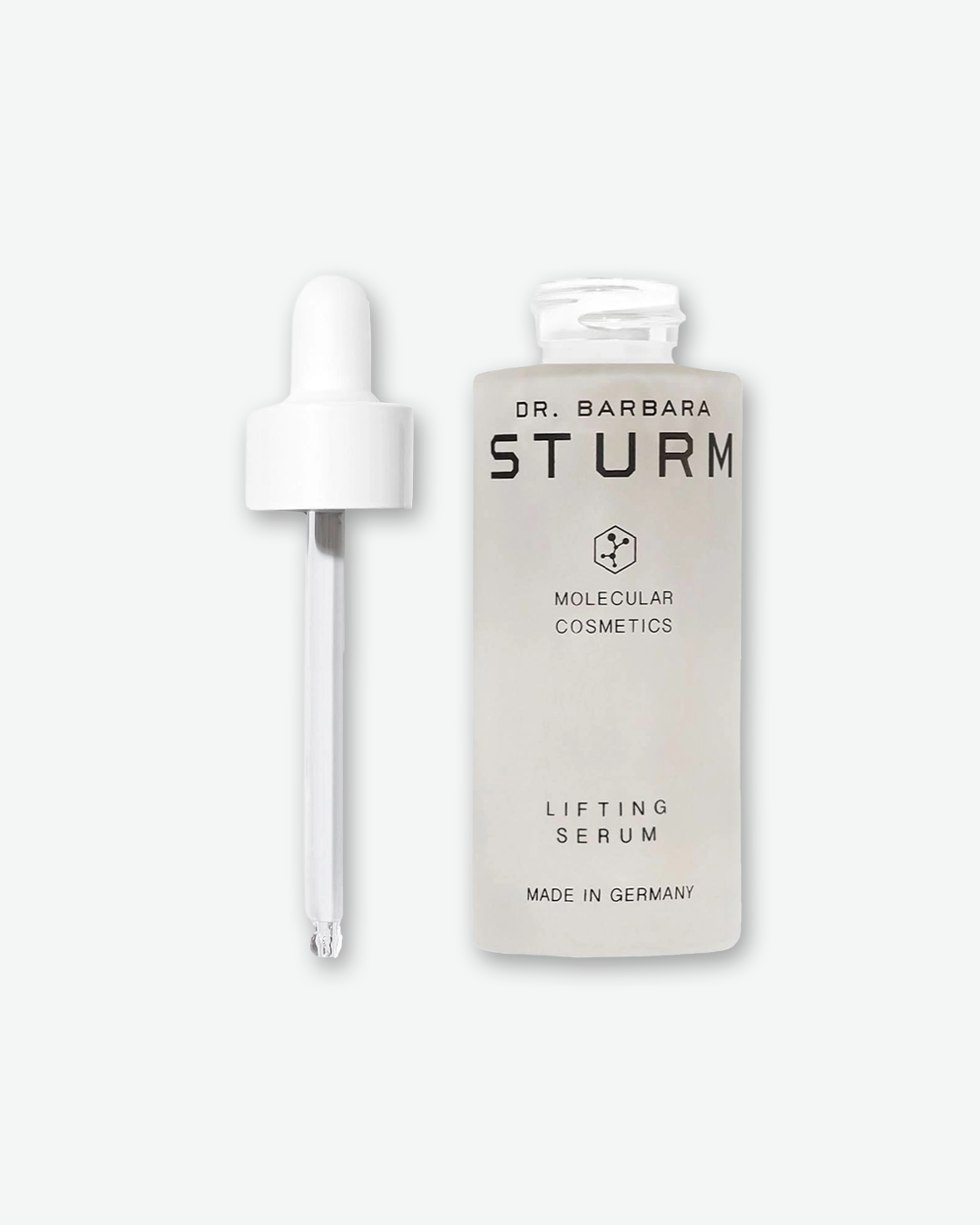 A product shot showing the Dr. Barbara Sturm Lifting Serum open on a light gray background. On the right stands the frosted glass bottle with its neck exposed. On the left, the white dropper wand is pulled out and stands upright, showing a clear glass pipette with a tiny droplet forming at the tip.