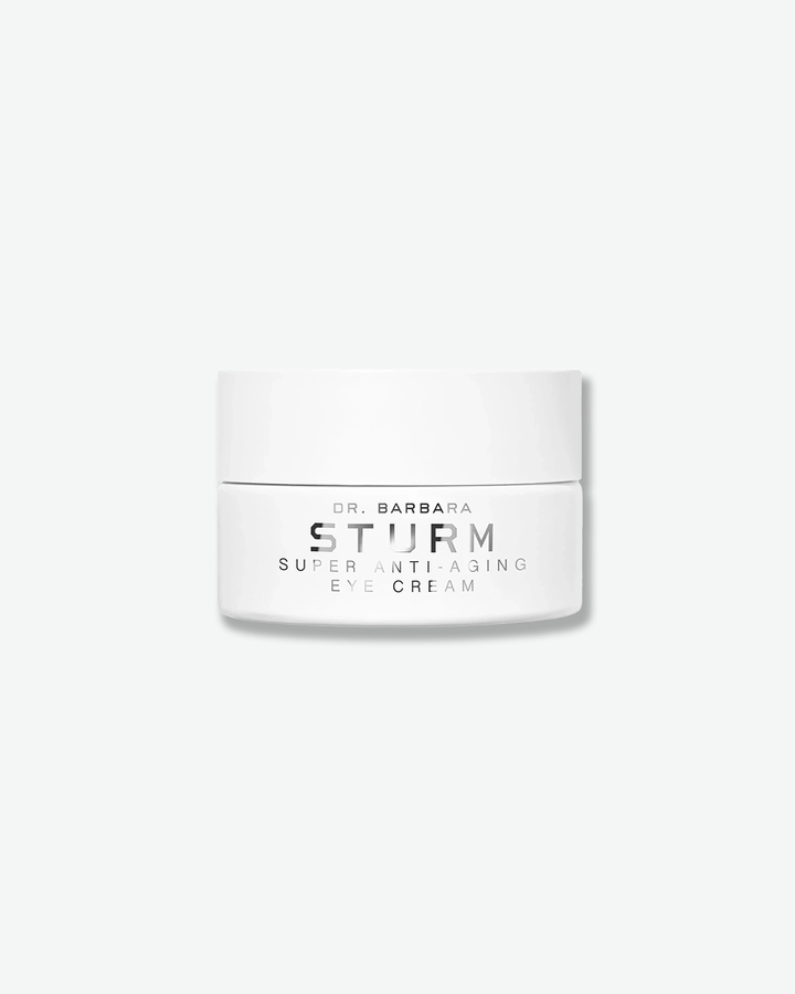 A product shot of a Dr. Barbara Sturm Super Anti-Aging Eye Cream jar, centered against a plain light gray background. The low, wide cylindrical jar is solid white with a matching flat screw cap. The front text reads "DR. BARBARA STURM", "SUPER ANTI-AGING", and "EYE CREAM" in clean black font.