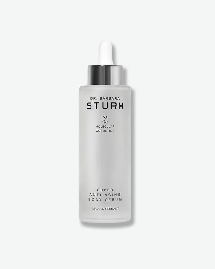 A tall, frosted glass dropper bottle of Dr. Barbara Sturm Super Anti-Aging Body Serum, standing vertically with a metallic silver cap and a white rubber bulb.
